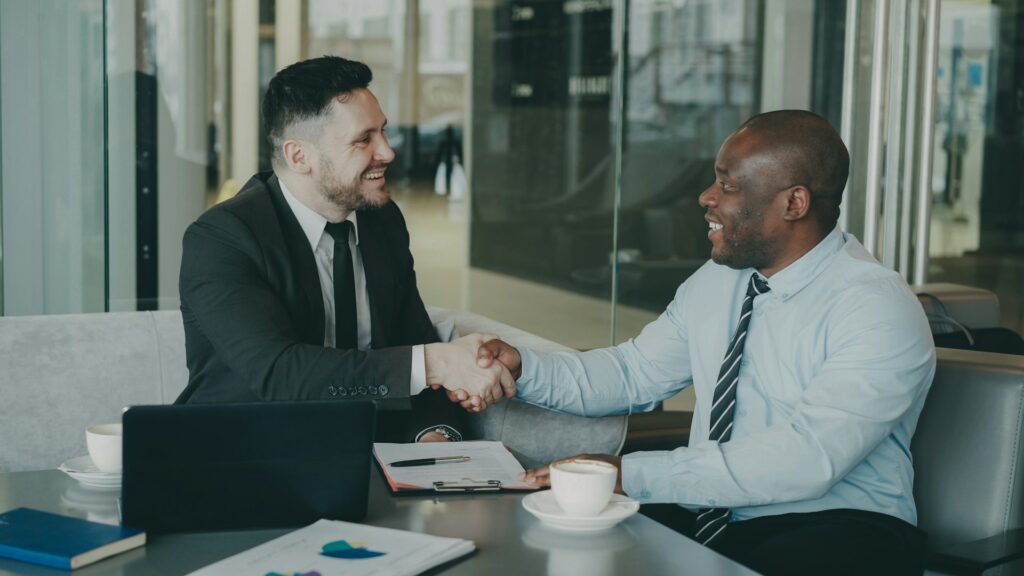 Business partners shaking hands across a conference table after a supplier meeting