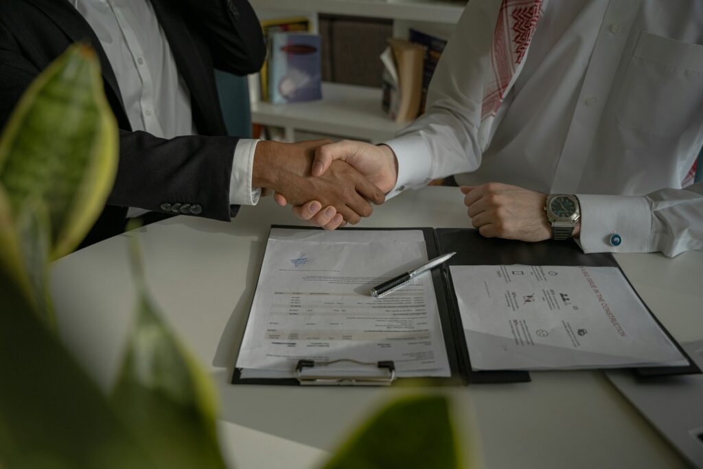 Business partners shaking hands over signed paperwork at a supplier meeting